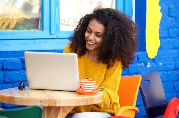 happy-young-woman-sitting-at-outdoor-cafe-using-PFFBJ93