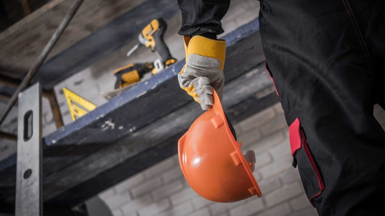 Hard Hat Construction Zone. Contractor with Orange Safety Hard Hat in Hand. Scaffolding with Tools in Background.