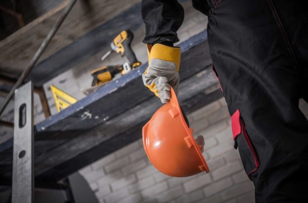 Hard Hat Construction Zone. Contractor with Orange Safety Hard Hat in Hand. Scaffolding with Tools in Background.