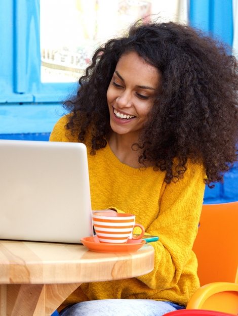 happy-young-woman-sitting-at-outdoor-cafe-using-PFFBJ93